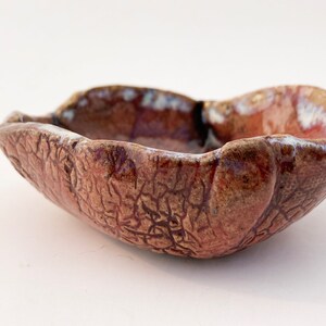 May include: A small, brown ceramic bowl with a textured, crackled glaze. The bowl has an irregular, organic shape and a slightly raised rim.