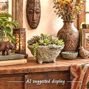 May include: A textured, light-colored ceramic planter with a wide, scalloped rim and three small feet, filled with a variety of green and reddish succulents, including a trailing string of pearls plant, positioned centrally in a decorative arrangement.