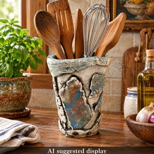 May include: A textured ceramic utensil holder with a mottled white, blue, and brown finish, containing a metal whisk and several wooden kitchen tools including a spoon and a slotted turner, standing upright on a wooden surface.