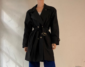 May include: A black double-breasted trench coat with a belt and gold buttons. The coat is worn over blue corduroy pants and white boots.