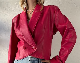 Puede incluir: Una chaqueta de cuero rosa brillante con cierre de doble botonadura y cuello ancho. La chaqueta tiene mangas largas y un corte corto.