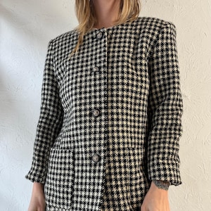 May include: A black and white houndstooth patterned blazer with a button-up front and a single pocket on the left side.