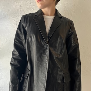 May include: A black leather blazer with a single button closure and two flap pockets. The blazer has a classic, tailored fit.