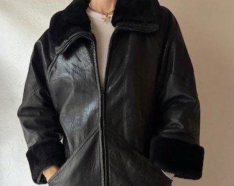May include: A black leather jacket with a faux fur collar and cuffs. The jacket has a zip-up front and two pockets. The sleeves have a textured design on the upper arm. The person is wearing red pants.