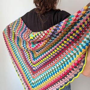 Pode incluir: Um xale de crochê colorido e feito à mão com capuz. O xale apresenta um design de quadrados da vovó em uma variedade de cores, incluindo rosa, azul, amarelo e marrom. As bordas são adornadas com uma borda ondulada amarela brilhante.