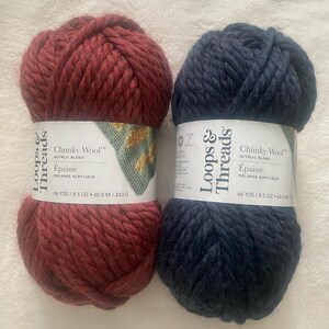 Puede incluir: Dos ovillos de hilo Loops & Threads Chunky Wool. Un ovillo es de color rojo oscuro y el otro es azul marino oscuro. Ambos ovillos están etiquetados con el nombre de la marca, el tipo de hilo y el metraje. La etiqueta también indica que el hilo es una mezcla acrílica.
