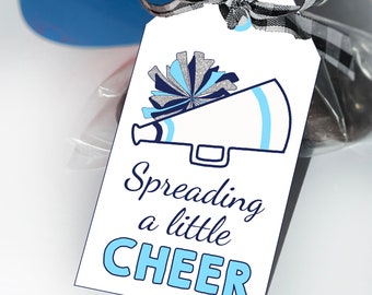 Puede incluir: Una etiqueta de regalo rectangular blanca con una ilustración de un pompón de animadora azul y plateado y un megáfono. El texto Spreading a little CHEER aparece en letras azul oscuro y azul claro. Una cinta de cuadros negros y blancos está atada arriba.