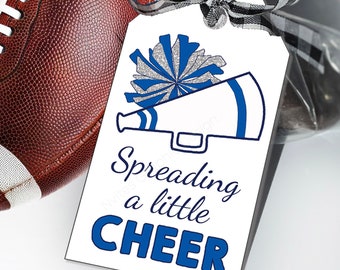 Puede incluir: Una etiqueta de regalo rectangular blanca con un gráfico de pompón azul y plateado brillante sobre una ilustración de megáfono azul. El texto dice Spreading a little CHEER en azul. Se incluye una cinta de cuadros vichy en blanco y negro.