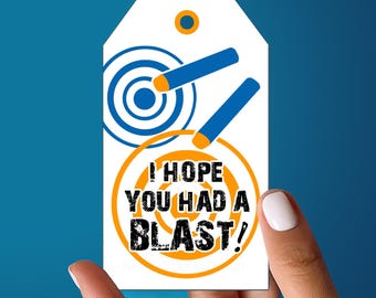 May include: A white rectangular gift tag with a hole at the top, featuring blue and orange target graphics and two blue darts with orange tips. The text "I HOPE YOU HAD A BLAST!" is printed in black, distressed, bold capital letters across the center.