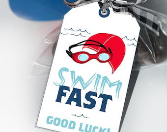 May include: A white gift tag with blue and white waves, a red swim cap, and blue goggles. The tag says "Swim Fast Good Luck!"
