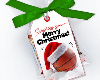 May include: A clear plastic treat bag tied with a green ribbon and a white gift tag. The tag features a basketball wearing a red and white Santa hat, with the text Swishing you a Merry Christmas! and a from: line printed in red and black ink.