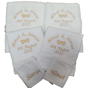 May include: A selection of white embroidered towels. The towels are embroidered with the names "Himat & Simran", the date "8th August 2022", and two hearts in gold thread. The set includes different sizes.
