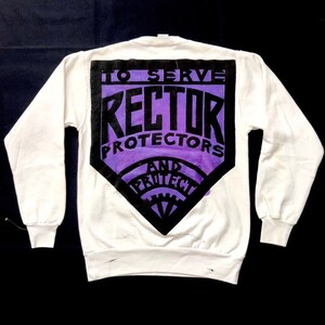 Puede incluir: Sudadera blanca con un gráfico en forma de diamante negro y morado en la espalda. El gráfico dice "To Serve", "Rector", "Protectors", y "And Protect".