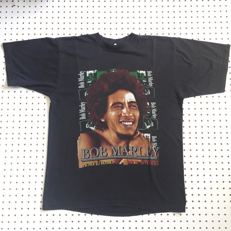 以下が含まれることがあります： ボブ・マーリーのカラフルな画像と「BOB MARLEY NATURAL MYSTIC」というテキストがプリントされた黒いTシャツ。