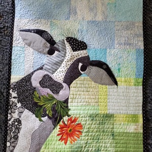 Puede incluir: Una colcha de retazos en blanco y negro con la cabeza de una vaca con una gran flor naranja en la boca. La colcha está hecha de varias telas y texturas, incluyendo un estampado floral y un patrón a cuadros. El fondo es un mosaico de cuadrados azules y verdes.