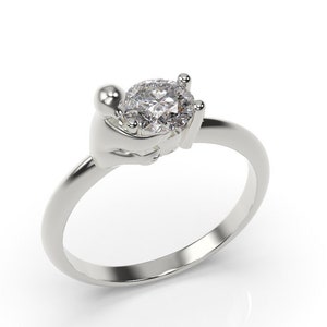 May include: A silver ring featuring a large, clear, round gemstone set in a distinctive design that resembles two hands holding the stone.