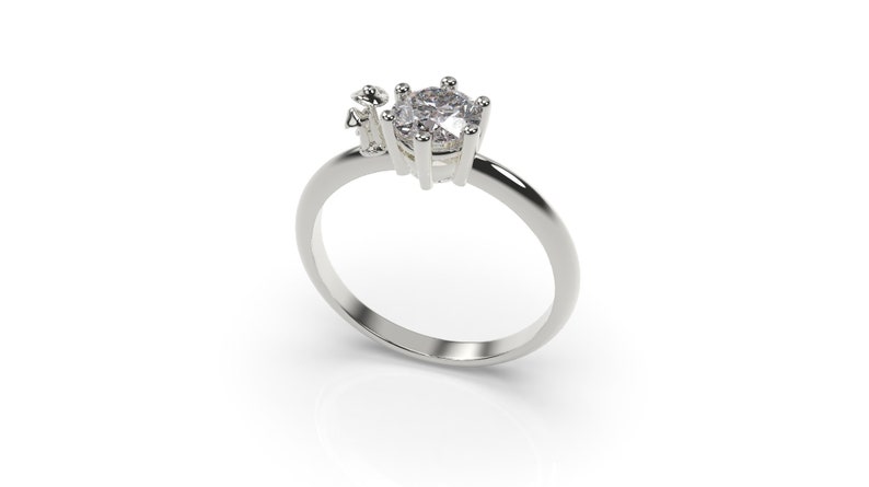 May include: A silver ring with a large, clear, round gemstone set in a prong setting. There are smaller gemstones on the side of the ring.