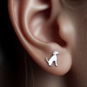 Pode incluir: Um par de brincos de pressão de prata com uma pequena silhueta detalhada de um cão.