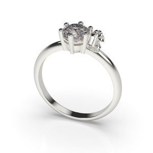 May include: A silver ring with a single large round clear stone and two smaller clear stones on the side.