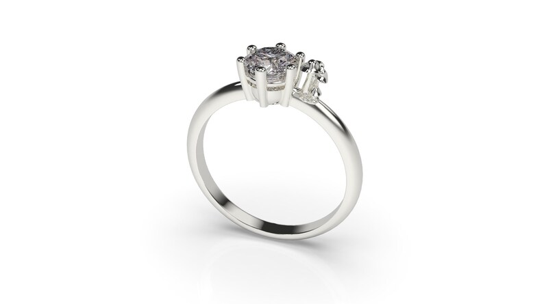 May include: A silver ring with a single large round clear stone and two smaller clear stones on the side.