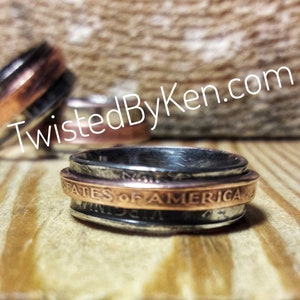 May include: A silver and copper ring made from stacked coins. The ring features the words "United States of America" on the copper band.