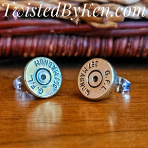 May include: A pair of gold-toned bullet casing earrings with silver posts. The casings are marked with "357 MAGNUM" and "G.F.L."