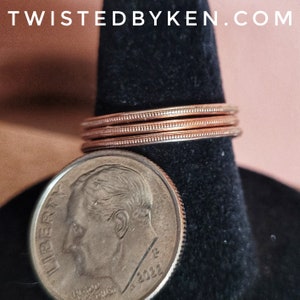 May include: A close-up of a stack of three copper rings on a black display stand. The rings are smooth and have a slightly textured surface. A US dime coin with the year 2022 is visible in the foreground.