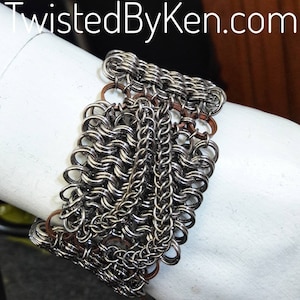 May include: A silver chainmail bracelet with copper accents. The bracelet is made of small, interlocking metal rings.