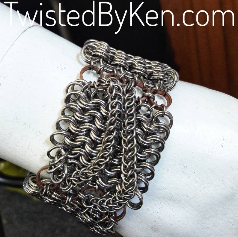 May include: A silver chainmail bracelet with copper accents. The bracelet is made of small, interlocking metal rings.