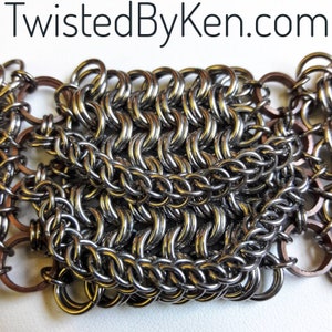 May include: Close-up of a silver chainmail bracelet with copper accents. The chainmail is made of small, interlocking metal rings.
