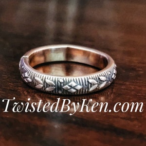 May include: A silver ring with a detailed geometric pattern. The ring is on a dark brown wooden surface.