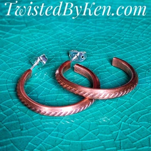 May include: A pair of copper hoop earrings with a textured design. The earrings are silver in color and have a post back closure.