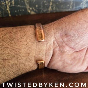 Puede incluir: Un brazalete de cobre martillado con un acabado texturizado. El brazalete est&aacute; abierto por los dos extremos y tiene una forma ligeramente curvada.