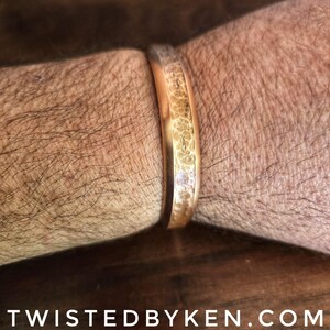 Puede incluir: Una pulsera de metal martillado de color dorado con una superficie texturizada.