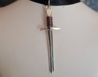 May include: A silver sword pendant with a copper-colored hilt, hanging from a black ribbon choker.