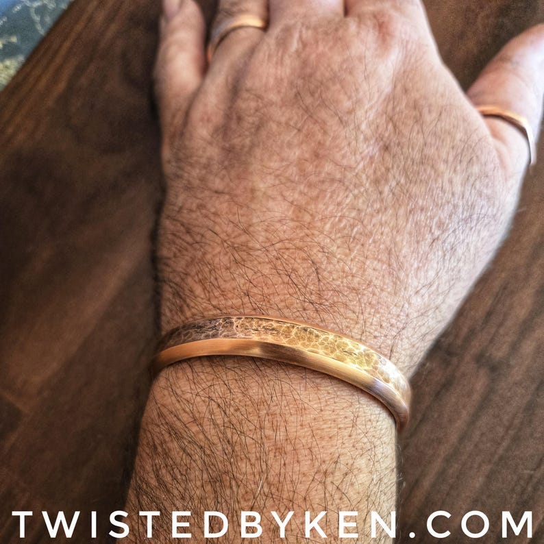 Puede incluir: Un brazalete de metal martillado de color dorado con una superficie texturizada. El brazalete se lleva en la mu&ntilde;eca de una persona.
