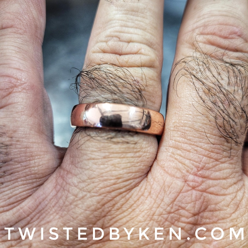 May include: A simple, polished, copper band ring worn on a finger.