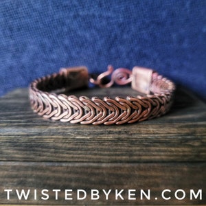 May include: A copper bracelet with a woven chain design. The bracelet is made of multiple strands of copper wire that are woven together to create a unique and intricate pattern.