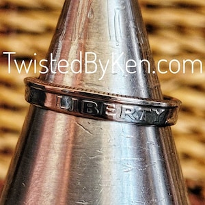 May include: A silver ring made from a US half dollar coin. The ring is engraved with the word "LIBERTY".