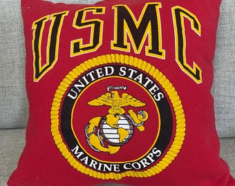 Może przedstawiać: Czerwona poduszka z czarno-żółtym emblematem USMC. Emblemat przedstawia glob, orła i kotwicę. Wokół emblematu widnieje napis "United States Marine Corps".