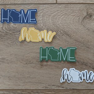 May include: Four different stickers with the word "home" and an outline of the state of Wisconsin. The stickers are in blue, yellow, green, and white.