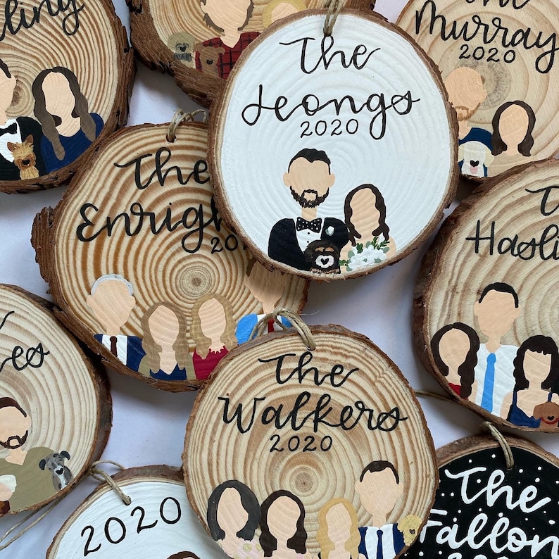 May include: A collection of personalized wood slice ornaments with painted portraits and names. The ornaments feature various family names, including "The Leongos 2020", "The Enrights 2020", "The Walkers 2020", and "The Fallon 2020".