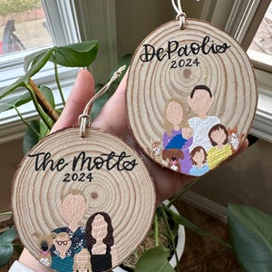 May include: Two round wooden ornaments with painted family portraits and the family names "The Motts" and "DePaolis" with the year 2024.