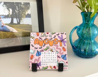 May include: A square desk calendar page for August featuring a light pink background with colorful illustrations of various insects including bees, beetles, snails, and dragonflies. The word August is written in large orange letters above a calendar grid.