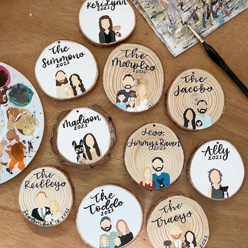 May include: Ten round wooden ornaments with painted portraits of families and their names. The ornaments are decorated with white paint and black lettering. The names include "The Simmono", "The Reilleyo", "Madison", "KeriLynn", "The Marplea", "Levo Jimmy & Raven", "The Jacobo", "The Toddo", "The Tracyo", and "Ally".