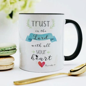May include: White ceramic mug with a black rim and handle. The mug has a watercolor design with the text "TRUST in the Lord with all your heart" and a red heart. The text "Proverbs 3:5" is also included.
