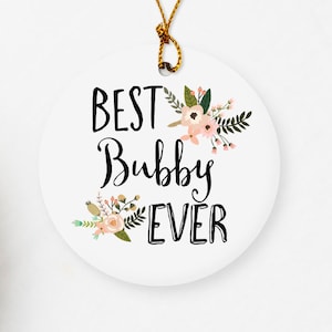 May include: White round ceramic ornament with a gold string. The ornament has a floral design and the text "BEST Bubby EVER" in black.