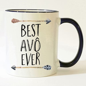 May include: White ceramic mug with a black rim and handle. The mug has a black and white arrow design and the text "BEST AVÔ EVER".