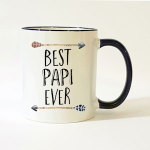 May include: White ceramic coffee mug with a black rim and handle. The mug has a black and white graphic of arrows and the text "Best Papi Ever".