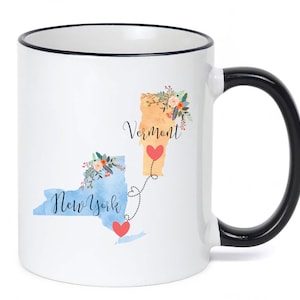 May include: White ceramic mug with a black rim and handle. The mug features a watercolor illustration of the states of New York and Vermont with the text "New York" and "Vermont" and a heart between the two states.
